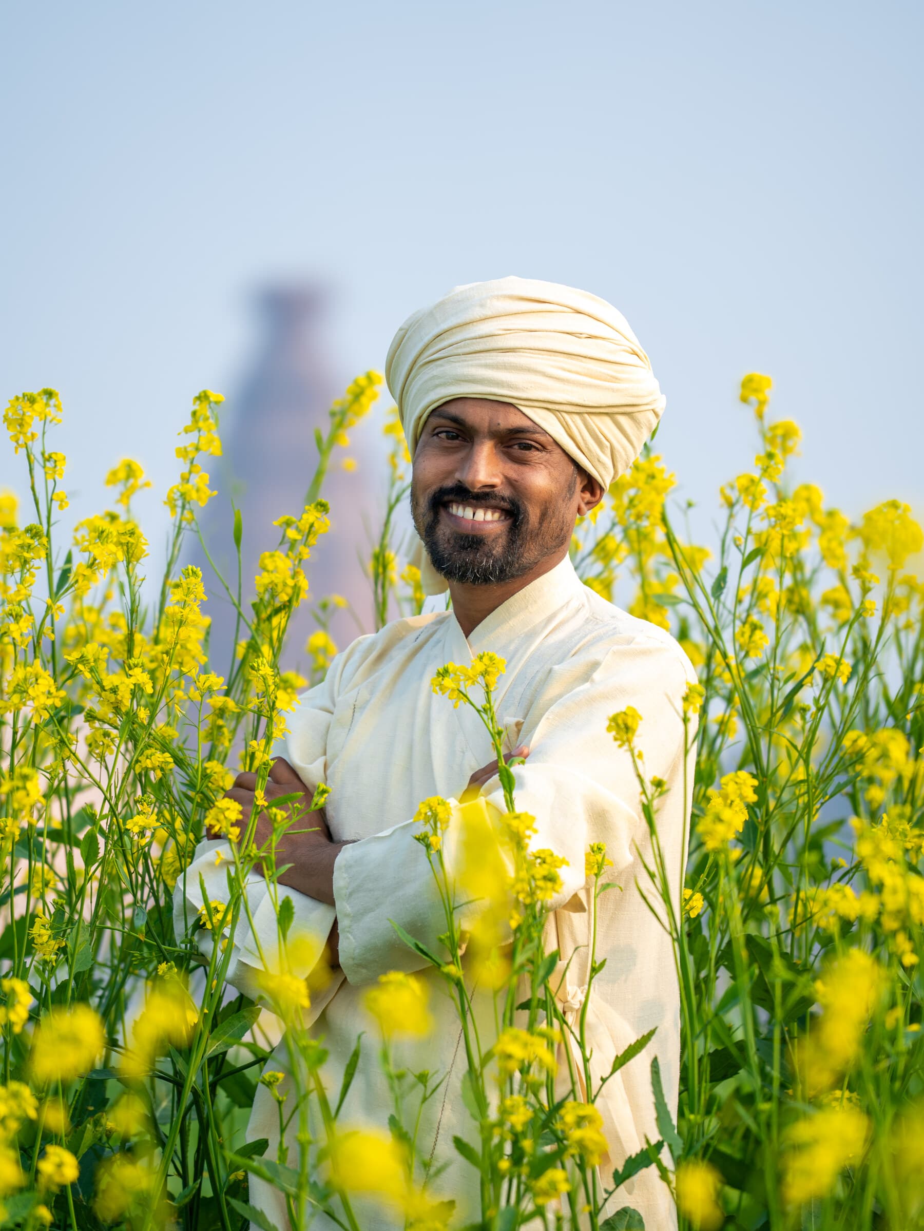 HH Paramguru Ji in a mustard flower field — joyful, warm, and present